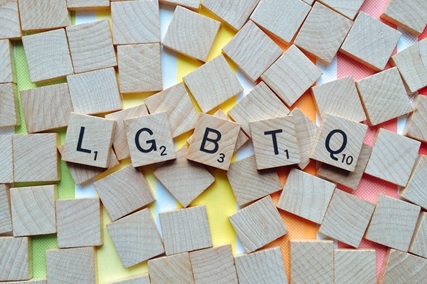 scrabble pieces on a rainbow background spelling L G B T Q