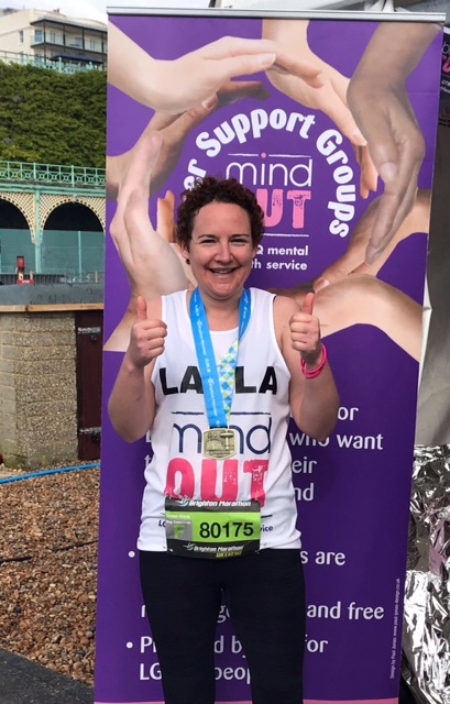 A smiling woman giving two thumbs up and wearing a medal for having just completed the Brighton Marathon 2018.
