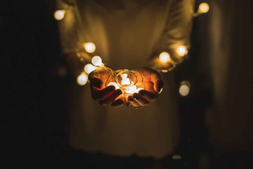person's hands together holding white fairy lights in a dark room