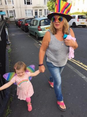 dawn wearing a rainbow top hat and sunglasses walking down the road with ella ray who is wearing rainbow butterfly wings