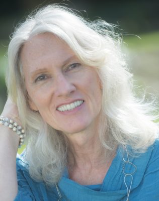 white woman with long white hair smiling at the camera wearing a blue top