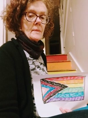 white woman holding a pride flag that she drew, sitting by the stairs