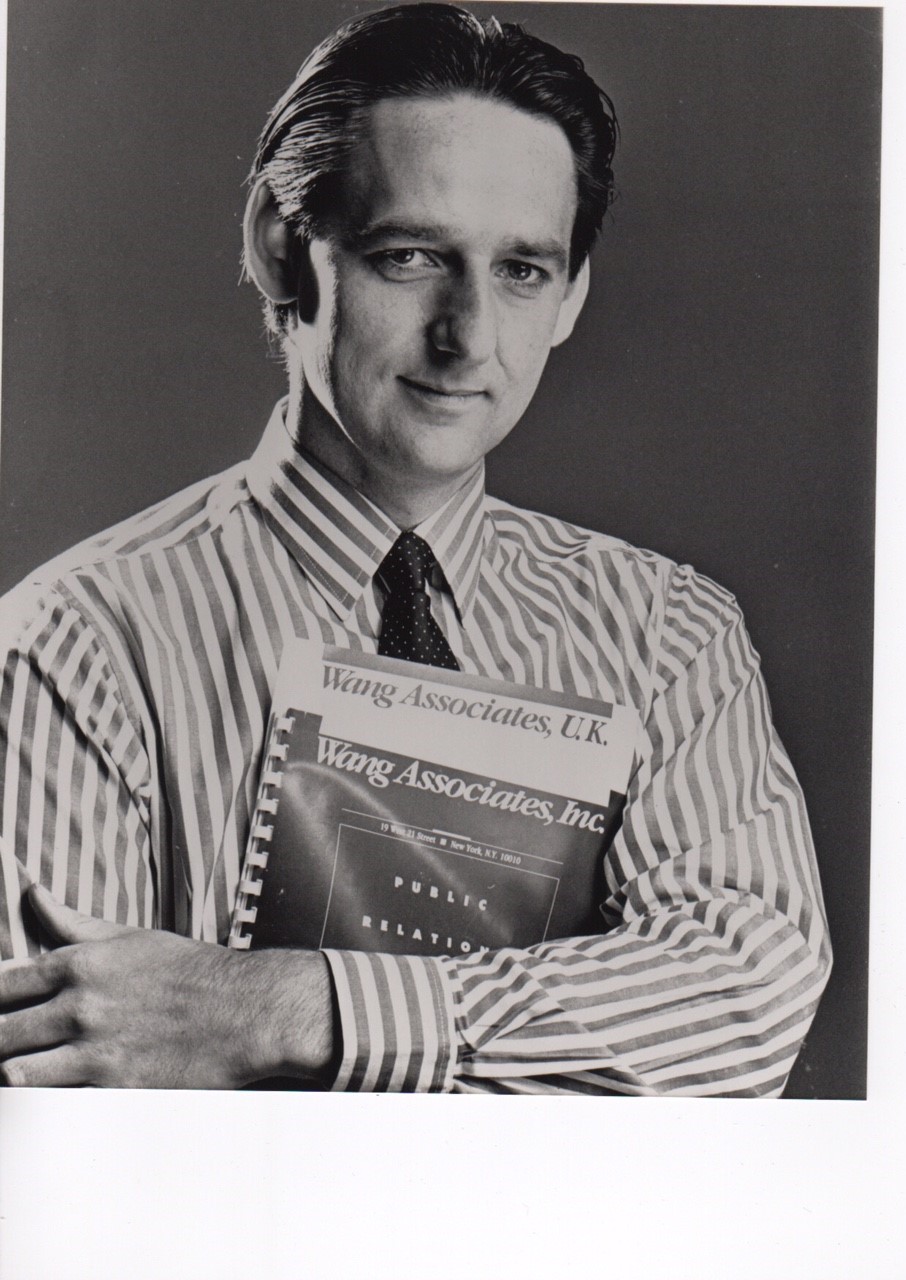 White man with dark hair, who's wearing a stripy shirt with a tie, and he's holding a book in his arms