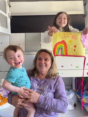 white woman, with two babies, one of them is holding a rainbow drawing