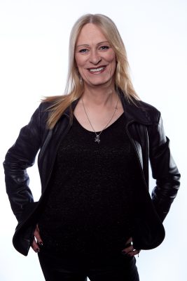 white feminine appearing person looking into the camera and smiling. They are wearing a black leather jacket and black top