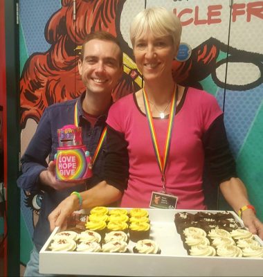 Two white appearing people holding cupcakes and smiling into the camera