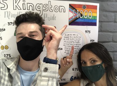 Two people wearing black masks pointing at the poster behind them