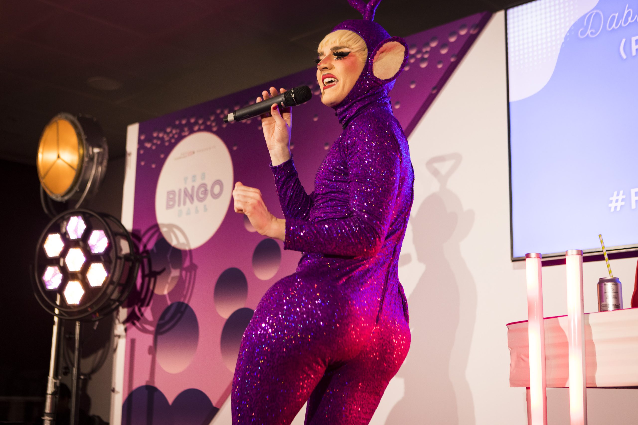 white appearing drag artist wearing a sequenced jump suit with their back towards the camera