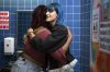 A non-binary femme embracing another student in a school bathroom