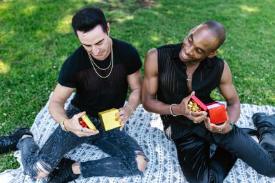two masc presenting people opening presents on the grass