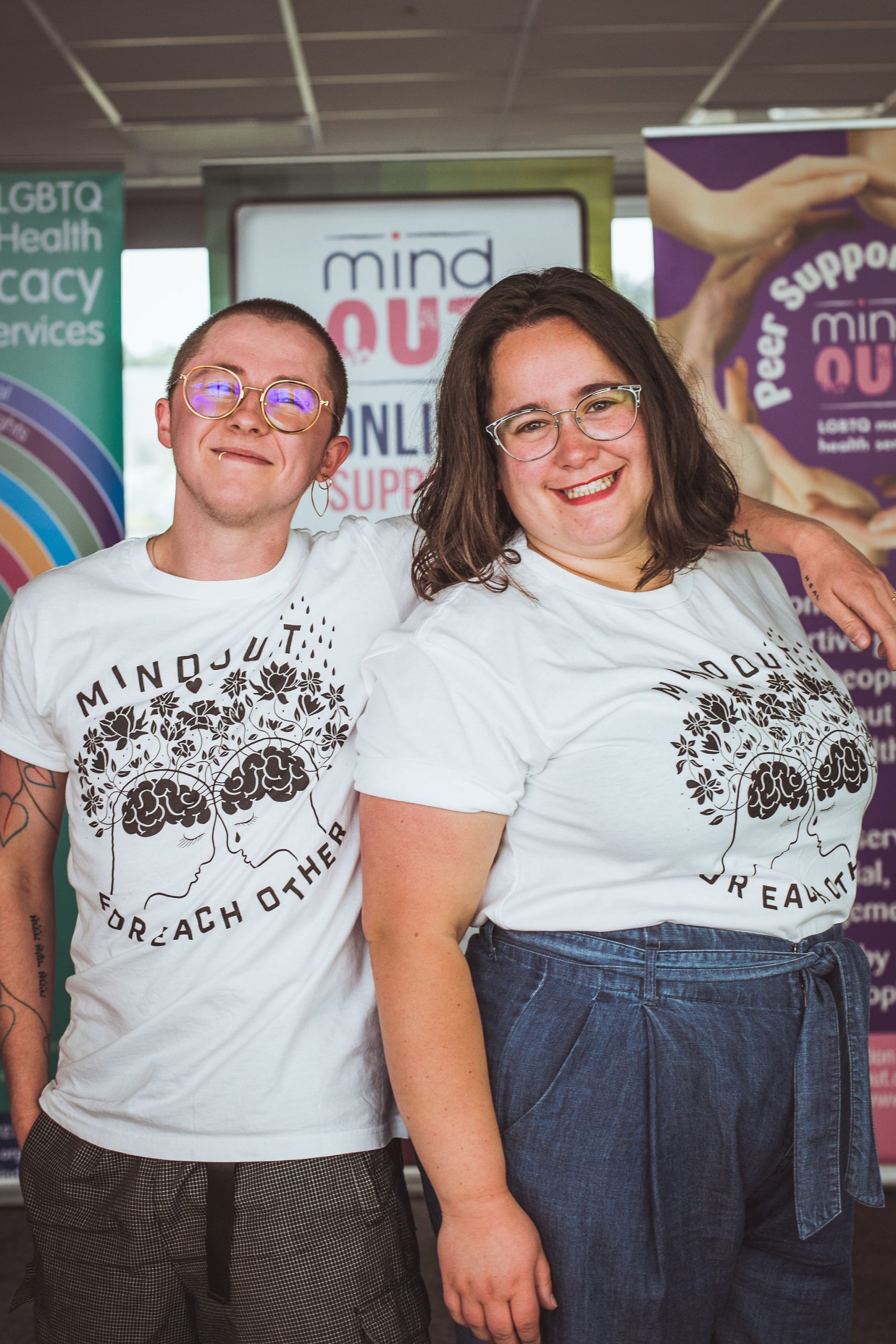 Kip and Gabi (MindOut staff) smiling into the camera wearing the new MindOut merch designed by Fox Fisher
