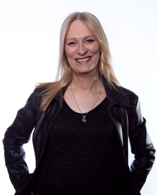 white feminine appearing person looking into the camera and smiling. They are wearing a black leather jacket and black top