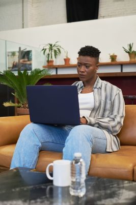Black person with short hair using a laptop while sitting on the sofa