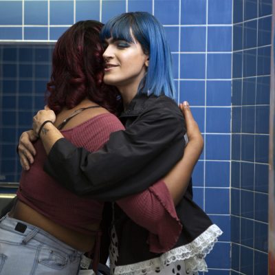 A non-binary femme embracing another student in a school bathroom