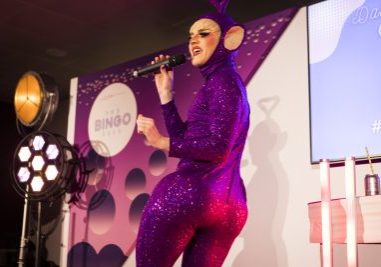 white appearing drag artist wearing a sequenced jump suit with their back towards the camera