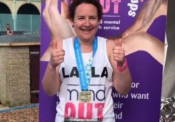 A smiling woman giving two thumbs up and wearing a medal for having just completed the Brighton Marathon 2018.