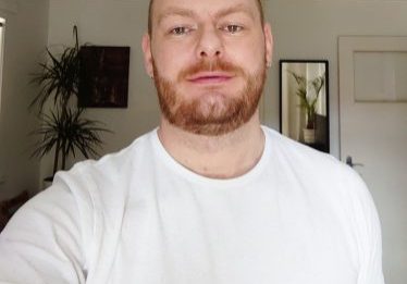 photo of person wearing a white t shirt, a plant and a full length mirror in the background