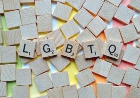 scrabble pieces on a rainbow background spelling L G B T Q